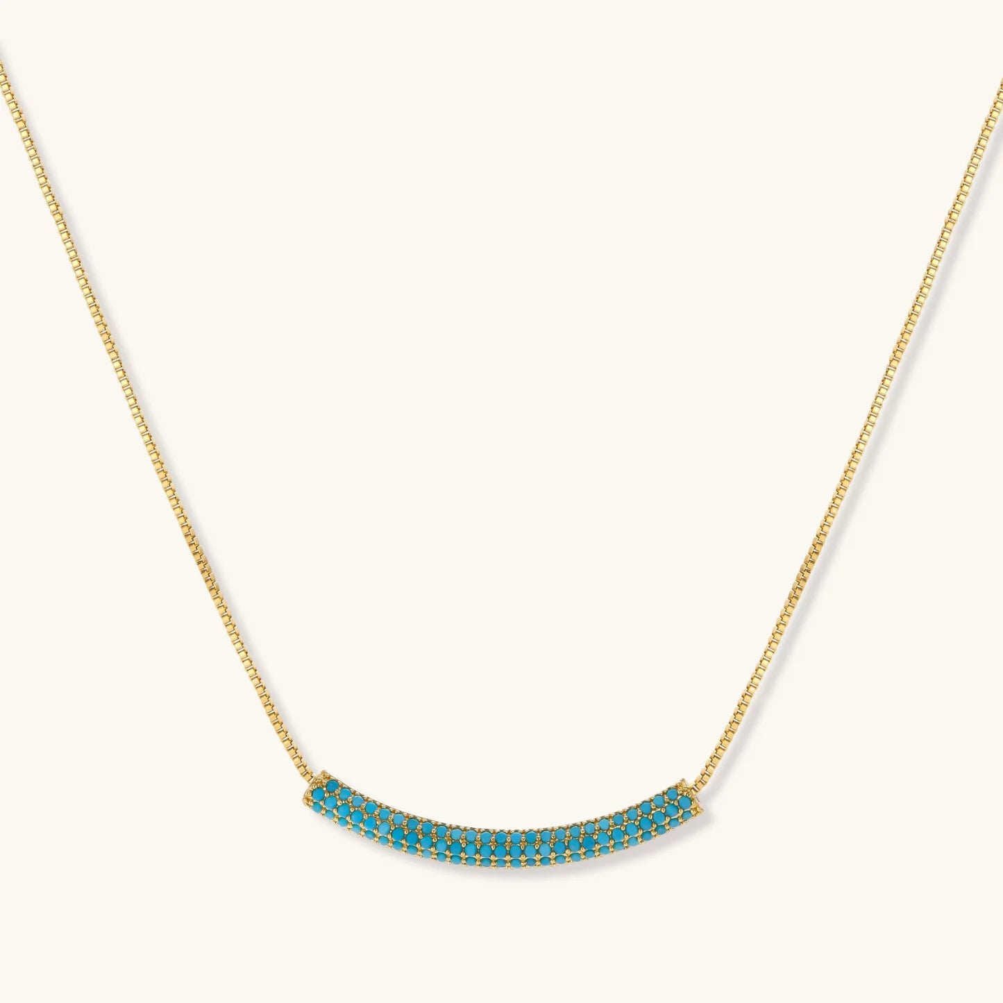 Gold-plated curved necklace and hoop earrings with turquoise cubic zirconia stones on white background.