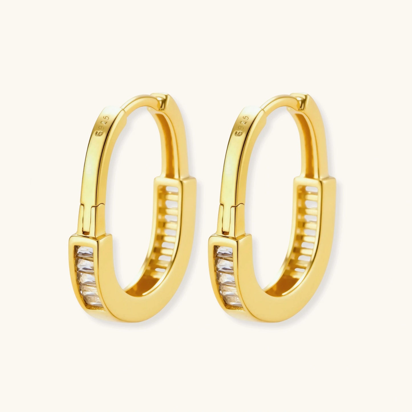 Close-up of gold-plated sterling silver huggie hoop earrings featuring rectangular cubic zirconia stones on neutral background.