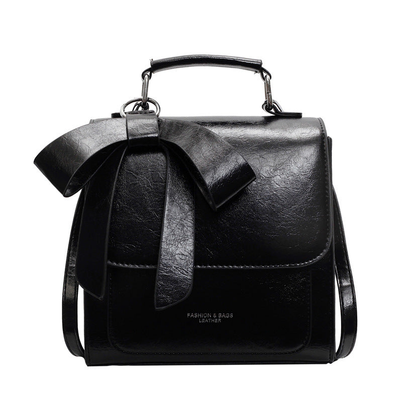 A creamy-white backpack with a bow design on the front, visible straps, and a zipper closure, held in a person's hand.