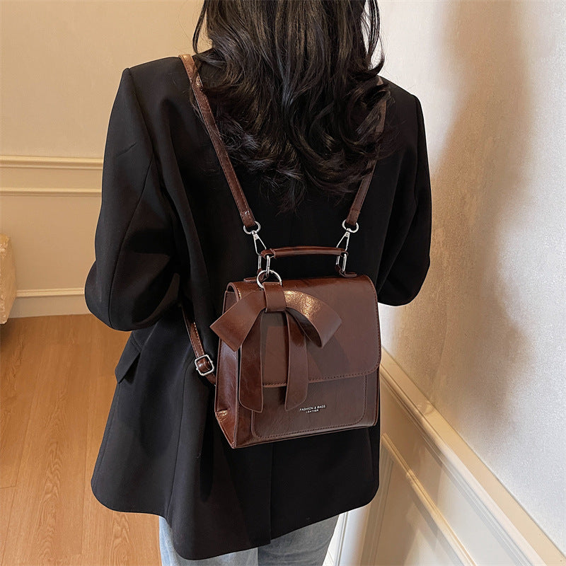 Person wearing a black coat with a brown leather backpack indoors.