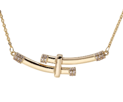 A gold bar necklace with a central T-shaped bar and small clear crystal accents on the ends, shown against a plain off-white background.
