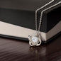 Silver love knot necklace with a sparkling cubic zirconia center, elegantly displayed against a polished wooden box background.