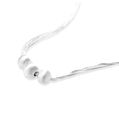 Sterling silver multi-strand necklace with three brushed round beads on cream background