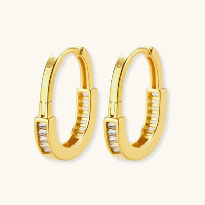 Close-up of gold-plated sterling silver huggie hoop earrings featuring rectangular cubic zirconia stones on neutral background.