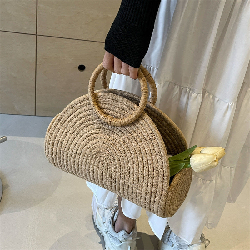 Person holding a woven handbag with a white tulip, wearing a black top and white pants.