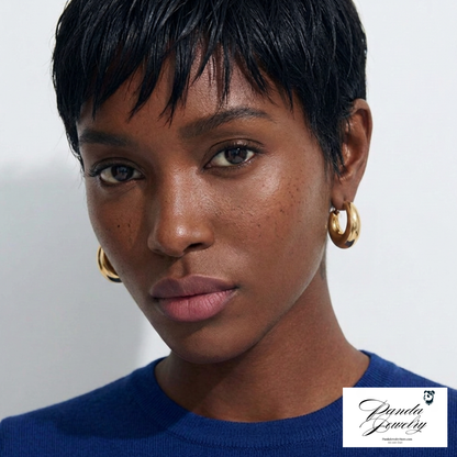 Close-up of a person wearing gold hoop earrings wearing a blue top with a neutral background