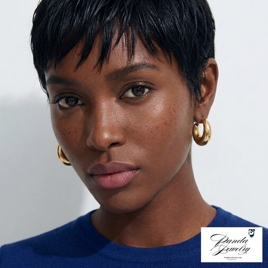 Close-up of a person wearing gold hoop earrings wearing a blue top with a neutral background