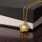 Gold love knot necklace with a sparkling cubic zirconia center, elegantly displayed against a polished wooden box background.