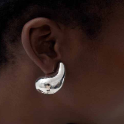A close-up image of a woman's ear wearing a silver, fluid, curved design stud earring.