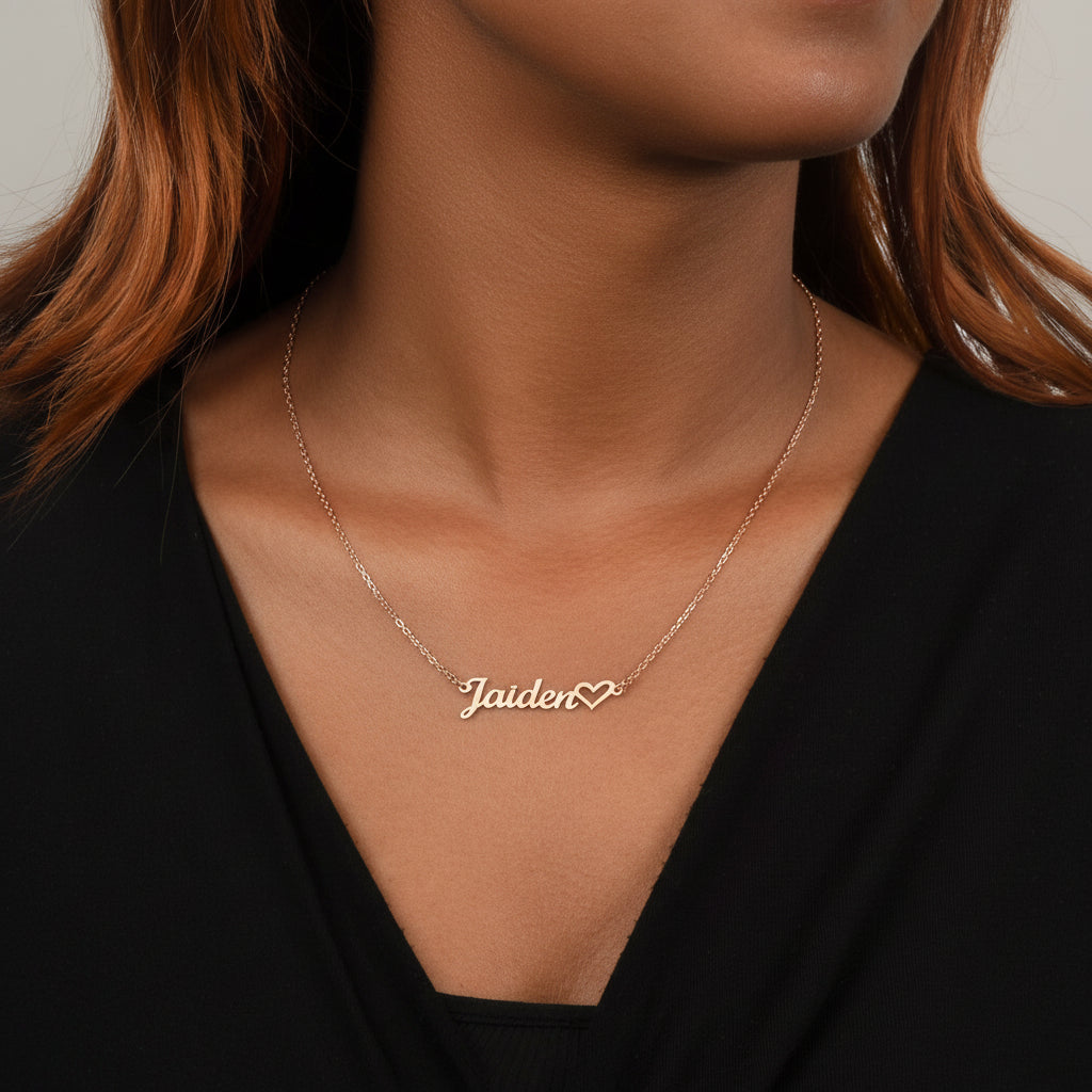 Person wearing a silver necklace with 'Jaiden' and a heart pendant on a plain background