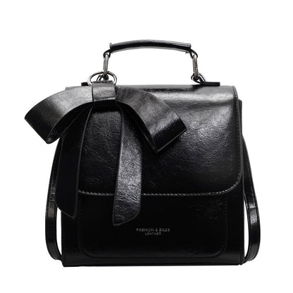 A creamy-white backpack with a bow design on the front, visible straps, and a zipper closure, held in a person's hand.