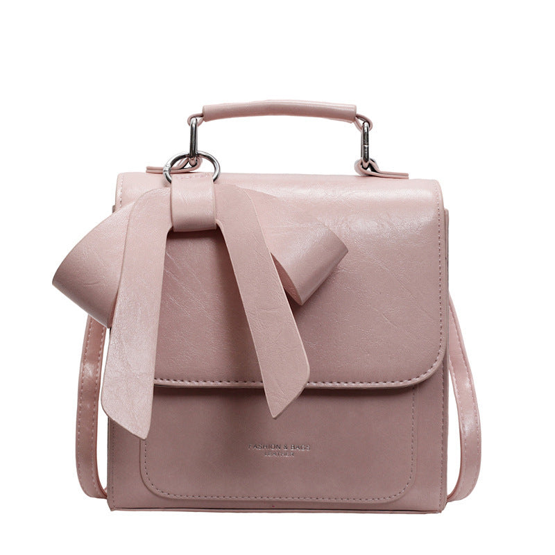 A creamy-white backpack with a bow design on the front, visible straps, and a zipper closure, held in a person's hand.