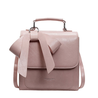 A creamy-white backpack with a bow design on the front, visible straps, and a zipper closure, held in a person's hand.