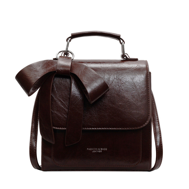 Brown leather handbag with a bow on a white background